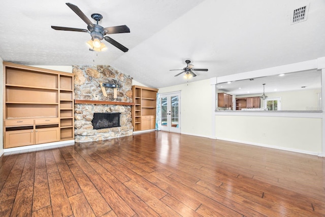 unfurnished living room featuring ceiling fan, hardwood / wood-style floors, a stone fireplace, vaulted ceiling, and french doors