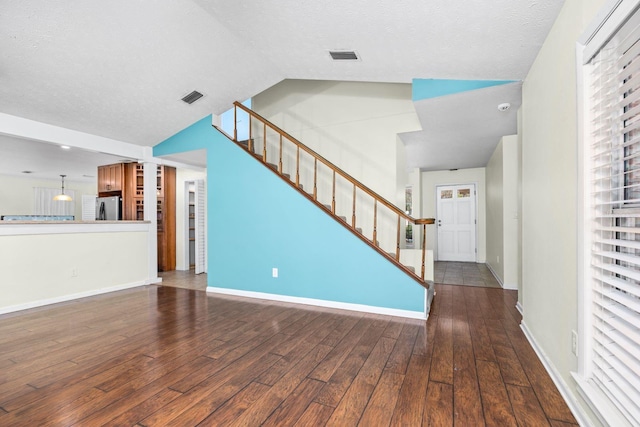 unfurnished living room with vaulted ceiling, a textured ceiling, and dark hardwood / wood-style flooring