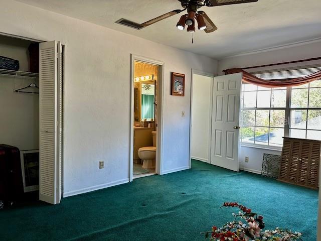 unfurnished bedroom with ceiling fan, ensuite bath, dark carpet, and a closet