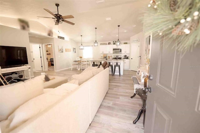 living room with vaulted ceiling, ceiling fan, and light wood-type flooring