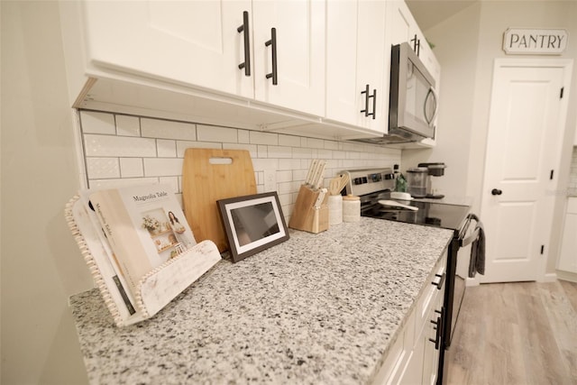 kitchen with white cabinetry, appliances with stainless steel finishes, backsplash, and light stone counters