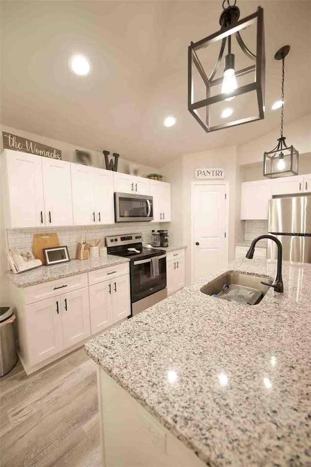 kitchen featuring sink, white cabinetry, light stone counters, hanging light fixtures, and stainless steel appliances