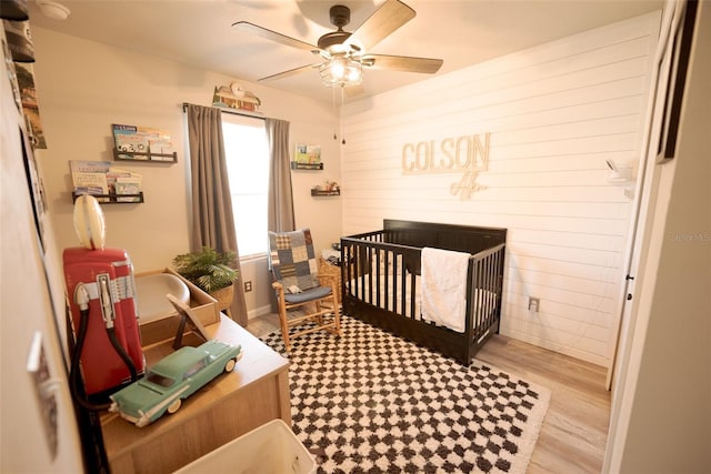 bedroom with a nursery area, ceiling fan, and light wood-type flooring