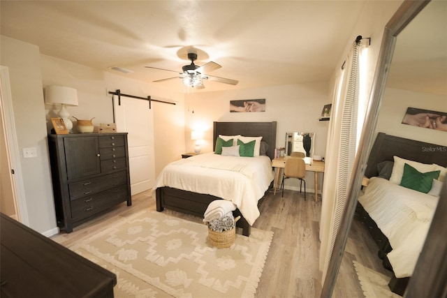 bedroom with a barn door, ceiling fan, and light wood-type flooring