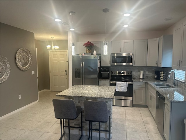 kitchen featuring appliances with stainless steel finishes, sink, hanging light fixtures, a center island, and light stone counters