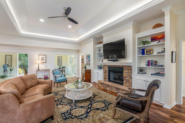 living room featuring built in features, ornamental molding, dark hardwood / wood-style floors, and a stone fireplace