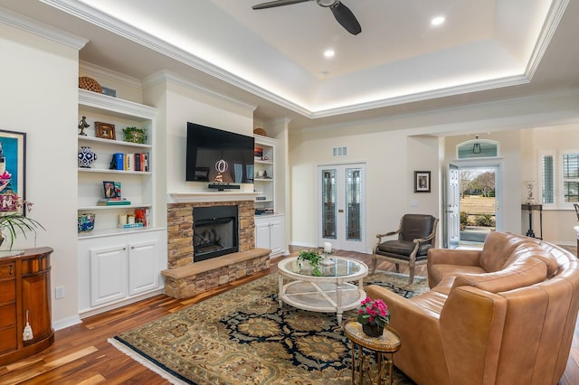 living room with a tray ceiling, a stone fireplace, ornamental molding, and hardwood / wood-style flooring