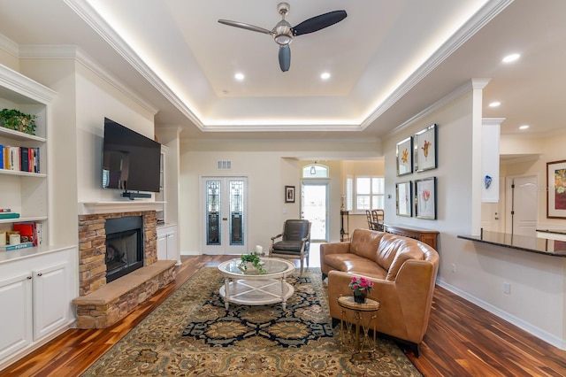 living room featuring dark wood-type flooring, crown molding, and a stone fireplace