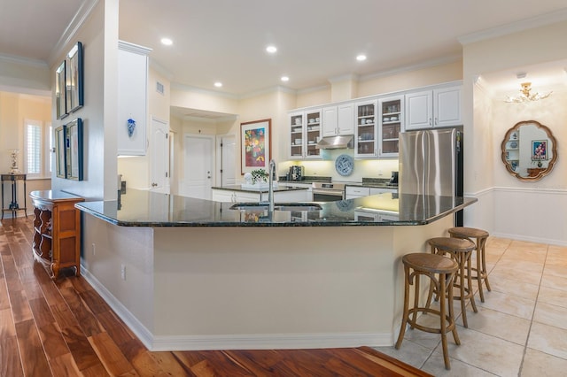 kitchen featuring a kitchen bar, sink, white cabinetry, stainless steel refrigerator, and dark stone counters