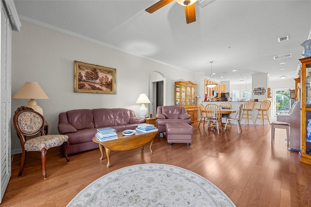 living room with ornamental molding, ceiling fan, and light wood-type flooring