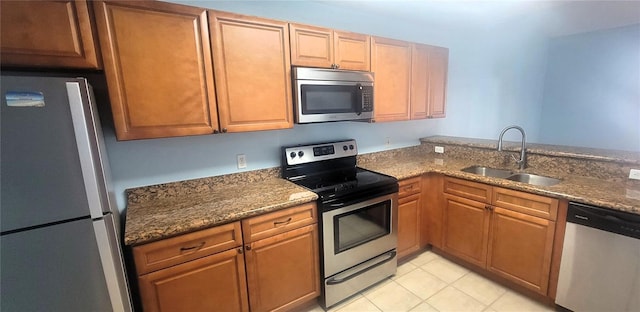 kitchen featuring appliances with stainless steel finishes, sink, dark stone countertops, light tile patterned floors, and kitchen peninsula