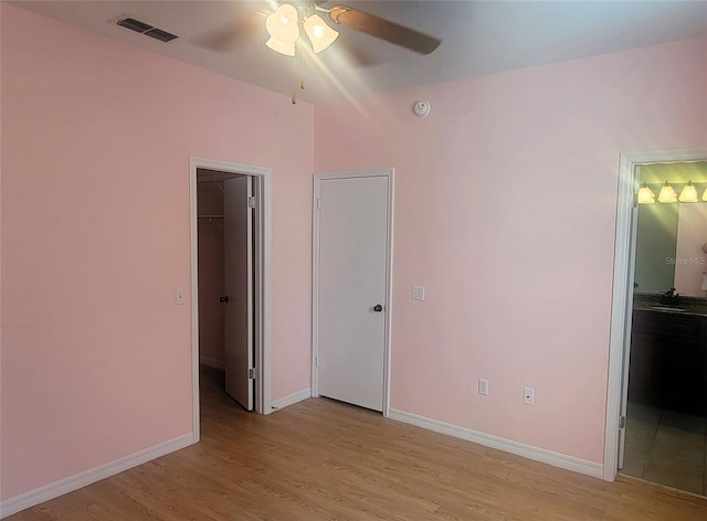 unfurnished bedroom featuring a walk in closet, ensuite bath, light hardwood / wood-style flooring, a closet, and ceiling fan