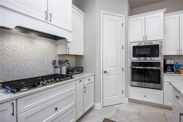 kitchen with appliances with stainless steel finishes, light stone countertops, custom range hood, and white cabinets