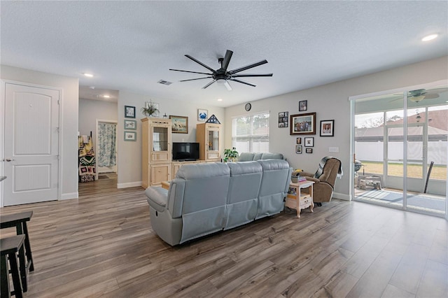 living room with a textured ceiling, wood-type flooring, and ceiling fan