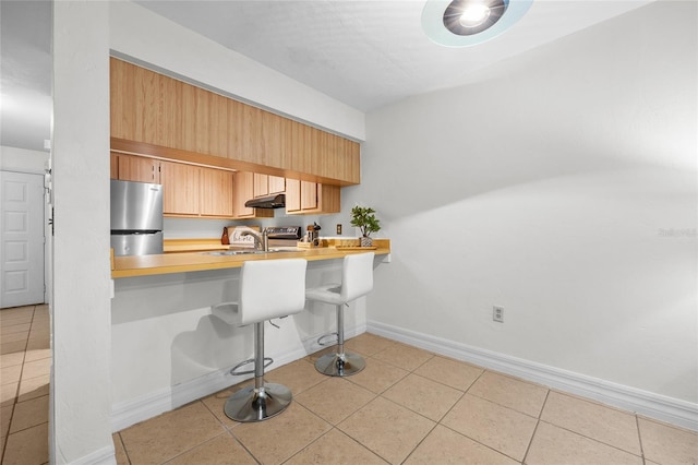 kitchen featuring stainless steel refrigerator, sink, a breakfast bar area, light tile patterned floors, and kitchen peninsula