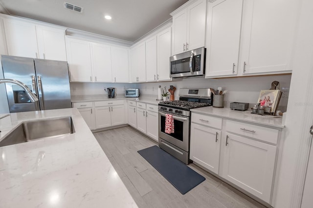 kitchen featuring sink, light stone counters, light hardwood / wood-style flooring, appliances with stainless steel finishes, and white cabinets