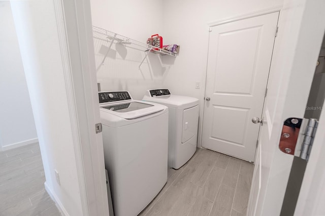 clothes washing area with washing machine and clothes dryer and light wood-type flooring