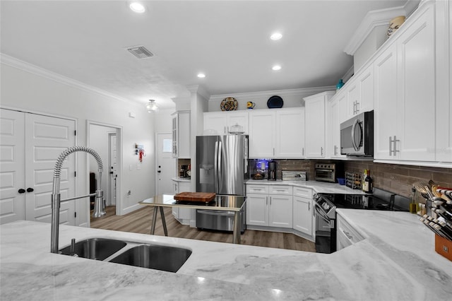 kitchen with sink, white cabinetry, light stone counters, appliances with stainless steel finishes, and backsplash