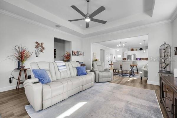 living room with a raised ceiling, ornamental molding, hardwood / wood-style flooring, and ceiling fan with notable chandelier