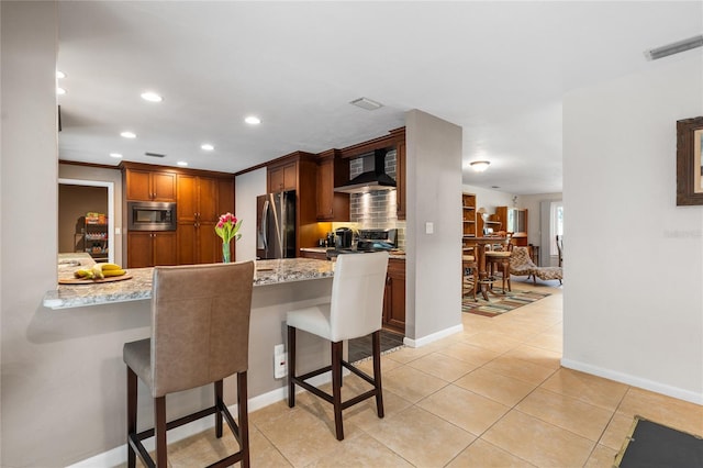 kitchen with wall chimney exhaust hood, appliances with stainless steel finishes, a peninsula, and a breakfast bar