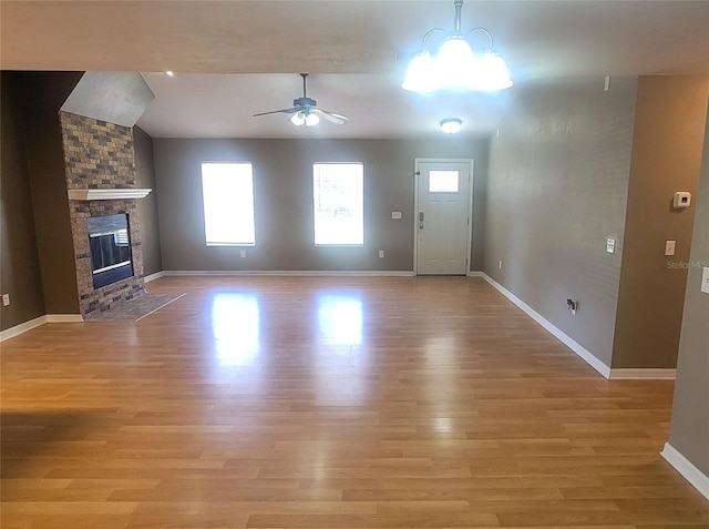 unfurnished living room featuring lofted ceiling, a fireplace, ceiling fan with notable chandelier, and light hardwood / wood-style flooring