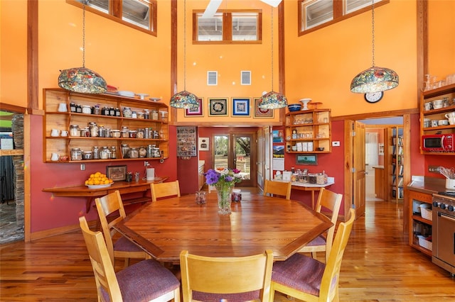 dining space featuring a towering ceiling, light wood-type flooring, and french doors