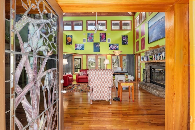 living area with hardwood / wood-style flooring, a towering ceiling, and a stone fireplace