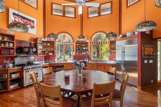 dining space with ceiling fan, sink, a high ceiling, and light wood-type flooring