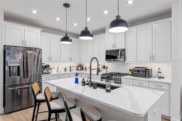 kitchen with stainless steel appliances, an island with sink, hanging light fixtures, and white cabinetry