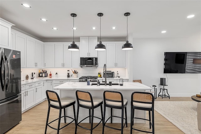 kitchen featuring black refrigerator, pendant lighting, white cabinets, and a center island with sink