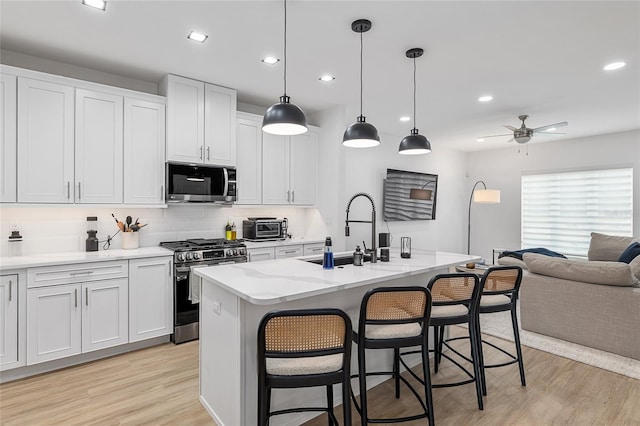 kitchen with a kitchen island with sink, decorative light fixtures, white cabinets, and appliances with stainless steel finishes