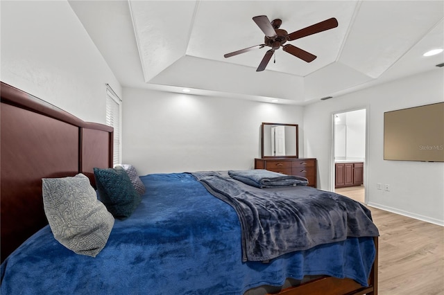 bedroom with ceiling fan, ensuite bathroom, light hardwood / wood-style floors, and a tray ceiling