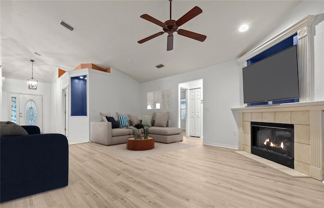 living room featuring ceiling fan, a tile fireplace, vaulted ceiling, and light hardwood / wood-style flooring