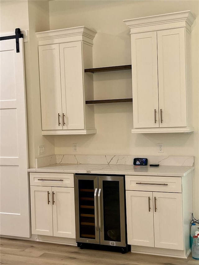 bar with light wood-type flooring, beverage cooler, a barn door, light stone countertops, and white cabinets