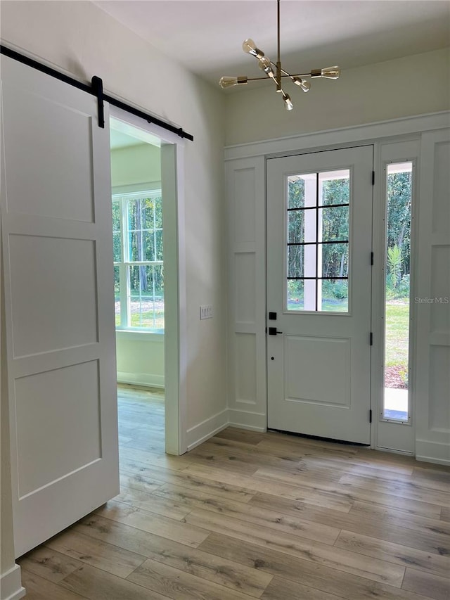 doorway to outside featuring a barn door, a chandelier, and light hardwood / wood-style flooring