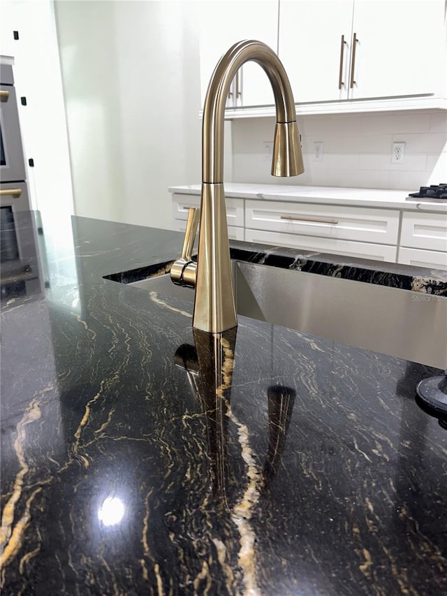 details featuring sink, dark stone countertops, and white cabinets