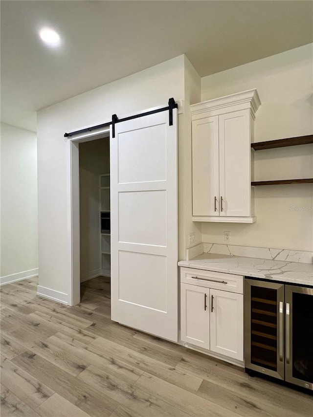 bar with white cabinets, wine cooler, a barn door, light stone countertops, and light wood-type flooring