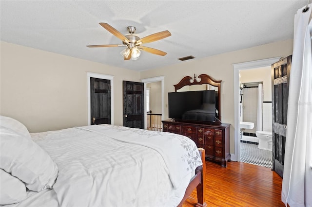 bedroom featuring ceiling fan, ensuite bathroom, hardwood / wood-style floors, and a textured ceiling