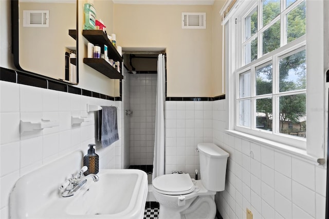 bathroom featuring plenty of natural light, toilet, sink, and tile walls