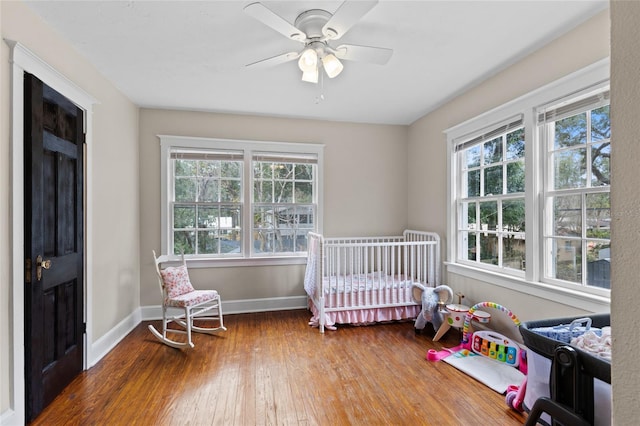 bedroom with multiple windows, hardwood / wood-style flooring, a nursery area, and ceiling fan