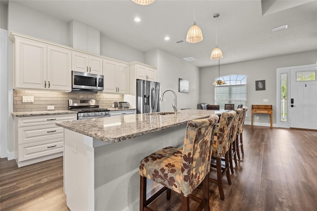 kitchen featuring pendant lighting, decorative backsplash, stainless steel appliances, and an island with sink