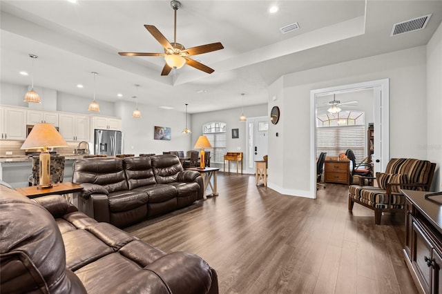 living room featuring a raised ceiling, ceiling fan, and dark hardwood / wood-style flooring