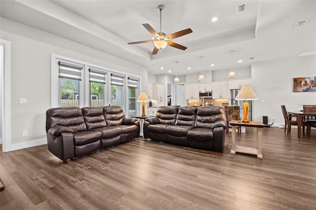 living room with ceiling fan, dark hardwood / wood-style floors, and a raised ceiling