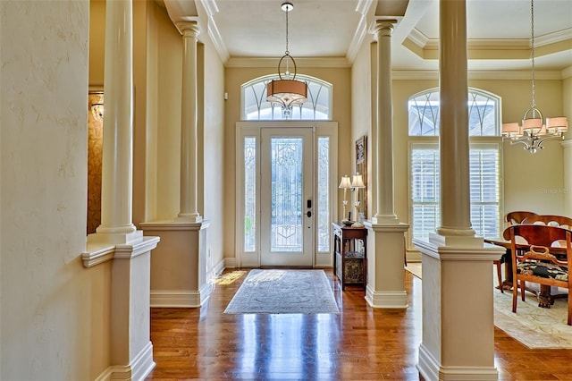 entryway with dark wood-type flooring, a notable chandelier, crown molding, and ornate columns