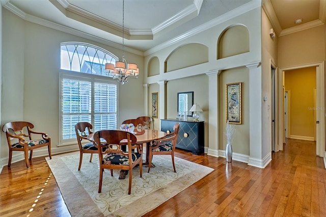 dining space with decorative columns, a notable chandelier, light hardwood / wood-style floors, a tray ceiling, and crown molding