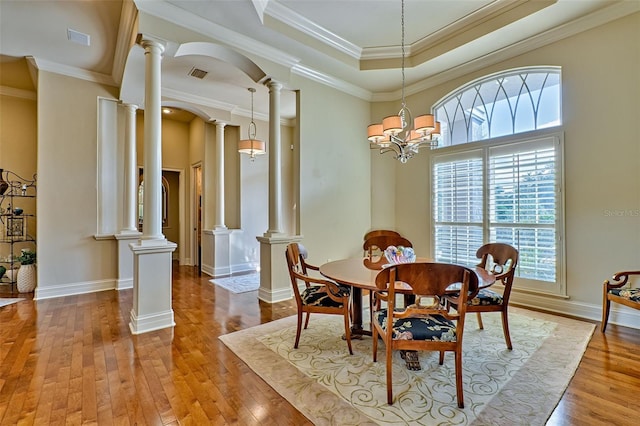 dining area featuring ornate columns, wood-type flooring, a raised ceiling, and ornamental molding