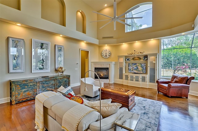 living room with ceiling fan, a high end fireplace, hardwood / wood-style floors, and a towering ceiling