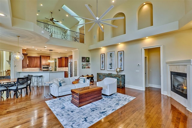 living room with a tiled fireplace, ceiling fan with notable chandelier, and light hardwood / wood-style flooring