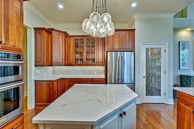 kitchen with ornamental molding, appliances with stainless steel finishes, a center island, and light stone counters