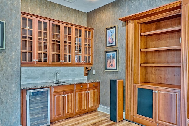 bar with sink, built in features, light stone counters, beverage cooler, and light wood-type flooring